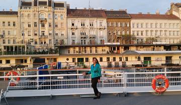 Person posing on a ship with a backdrop of European architecture.