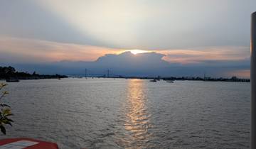 Sunset over a river with boats and a bridge in the distance.