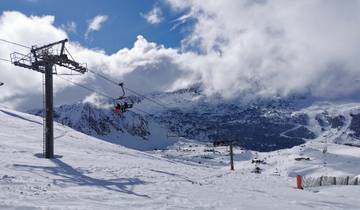 Snowy mountain ski area with ski lifts and cloudy skies.