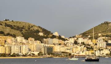 Coastal cityscape with boats and buildings against a mountainous backdrop.