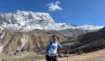 Hiker with a stick on a mountain trail with snowy peaks.