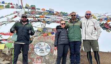 Hikers posing with prayer flags on a mountain summit.