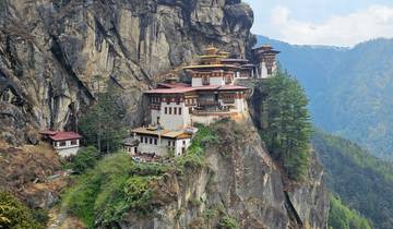 Monastery perched on a cliff surrounded by lush greenery.