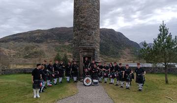 Group of bagpipers standing in front of a tall stone tower.