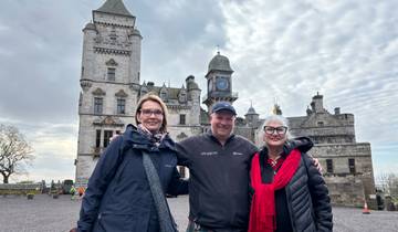 Three people standing in front of a historic castle.