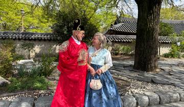 Couple in hanbok posing with traditional architecture in the background.
