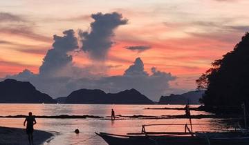 Beautiful sunset at a beach with people and mountains in the background.