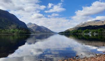 Reflective lake surrounded by mountains under a blue sky.