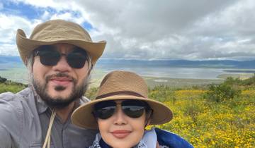 Two people posing in front of a scenic landscape with yellow flowers.