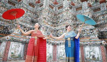 Two women in traditional dress with umbrellas in front of decorative temple.