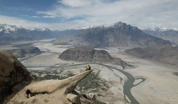 Two people sitting on a rock with a panoramic mountain view.