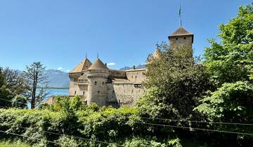 A castle by a lake with mountains in the background.