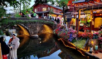 Scenic view of a traditional bridge over a stream with flowers and people.