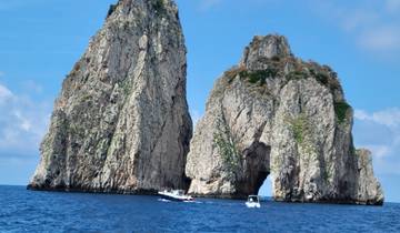 Two large rocky cliffs rising from the sea with boats nearby.