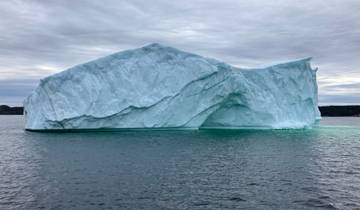 A large iceberg floating in the ocean under a cloudy sky.