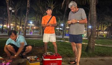 Three people having a picnic near palm trees, with string lights visible.