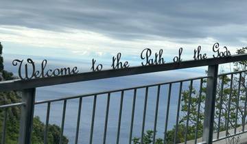 A sign reading 'Welcome to the Path of the Gods' with a sea view.