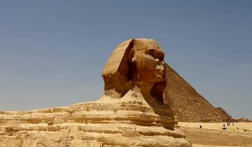 The Sphinx with a pyramid in the background under a clear sky.