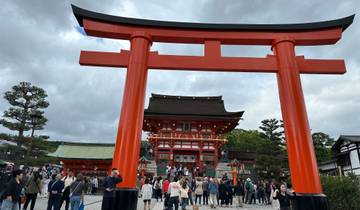 People walking under a large red torii gate at a temple complex.