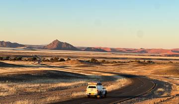 Car on a winding road with red desert hills in the background.