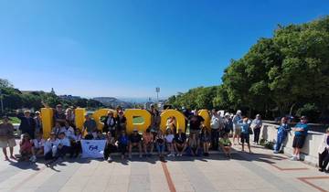 Group of people posing in front of 'Lisboa' sign with city view.