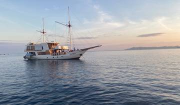 Sailing boat on calm waters at sunset with an island in the distance.