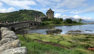 Eilean Donan Castle surrounded by greenery and a stone bridge.