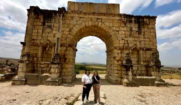Two people standing under an ancient stone archway.