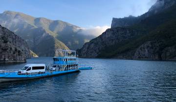 Blue ferry carrying a van on a scenic lake surrounded by mountains.
