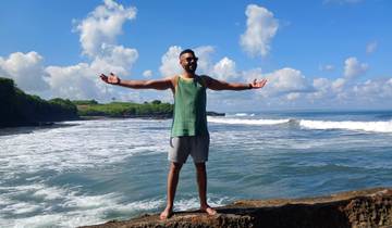 Person standing with arms outstretched on a rocky shore.