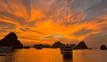 Golden sunset over Halong Bay with silhouettes of boats and karst formations.