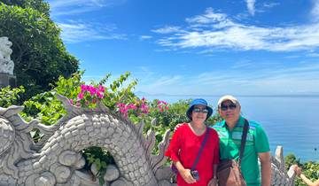 Couple posing by a detailed sculpture with an ocean view.