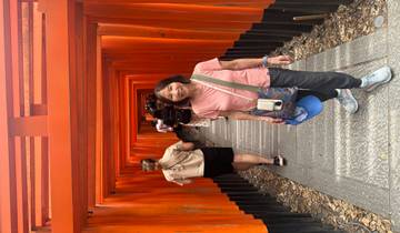 Tourist smiling in a corridor lined with red wooden torii gates.