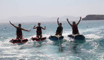 Four people on inflatable tubes being towed in the sea.