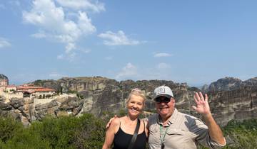 Couple waving with Metéora rocks and monasteries behind.