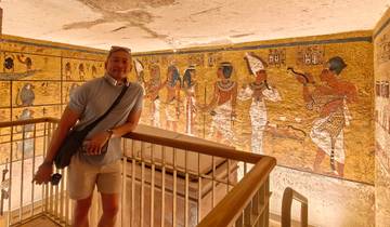 Tourist posing next to colorful Egyptian wall art.