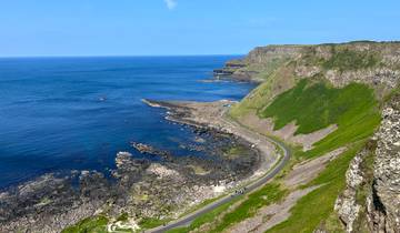 Scenic coastal view with lush cliffs and a winding road.