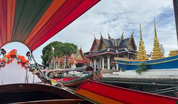 Colorful longtail boat passing by ornate structures by the river.