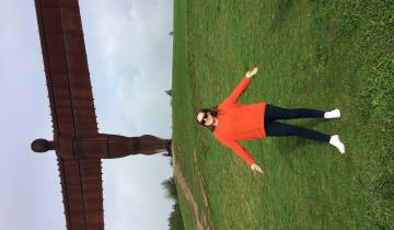 A woman posing with arms open in front of a large sculpture.