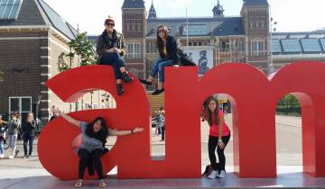 Four people posing with large letters in a public square.