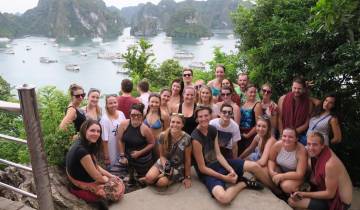 Large group posing in front of scenic bay view with boats.