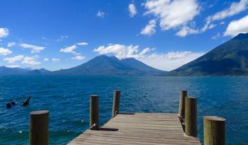 A dock extending into a clear blue lake with mountains.
