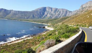 Scenic coastal road with ocean and mountain views.