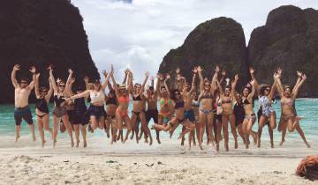 Group of friends jumping on the beach with scenic cliffs.