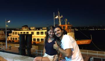 Two people posing in front of a large ferry during nighttime.