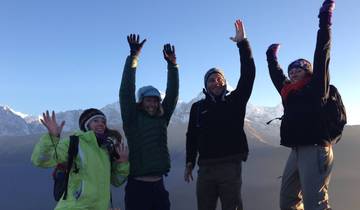 Group of people in winter attire, raising hands joyfully with snowy mountain backdrop.