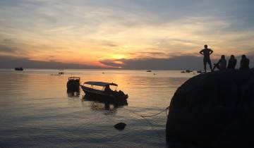 Silhouettes of people and boats against a vibrant sunset.