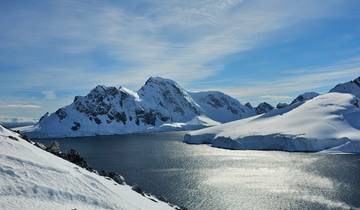Snowy mountain landscape with bright sun and water.