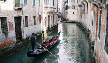A gondola being rowed in a narrow canal with historical buildings.