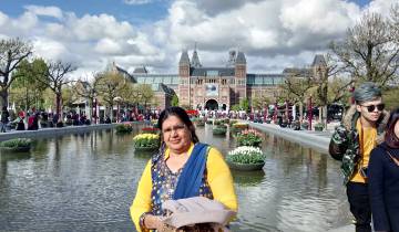 Woman posing in front of a fountain and museum in Amsterdam.